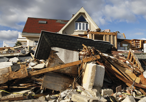 daños causados por un huracán y una montaña de escombros frente a una casa con techo rojo